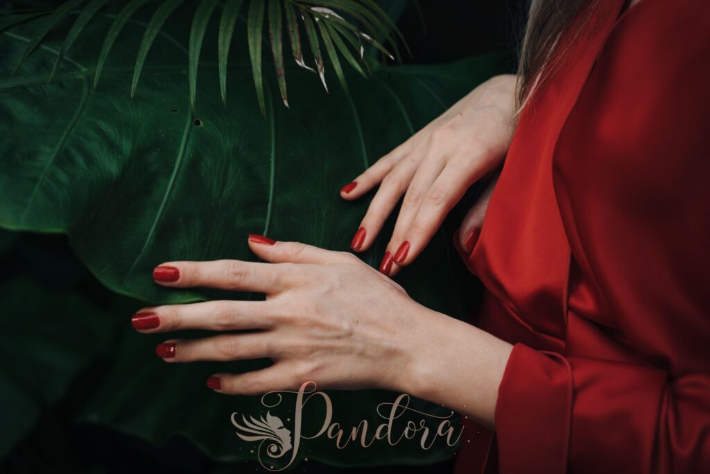Close-up shot of manicured hands with red nails resting on a large green leaf — Pandora Nail Spa, Lafayette, CA