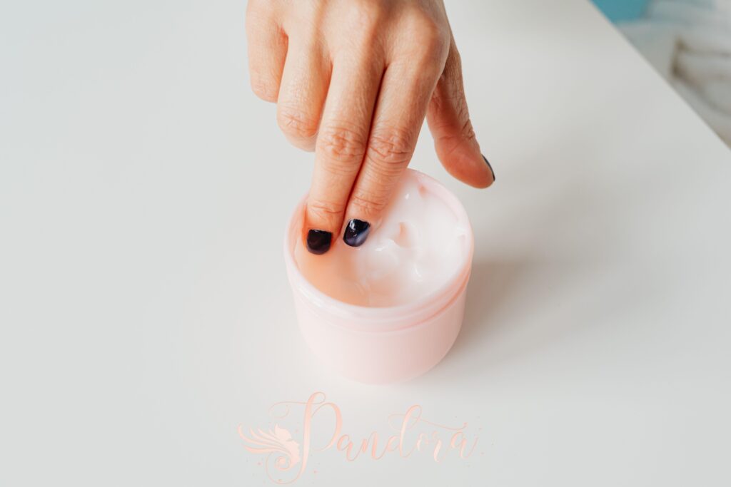 Close-up of a hand with painted nails dipping into a jar of face cream, representing self-care — Pandora Nail Spa, Lafayette, CA
