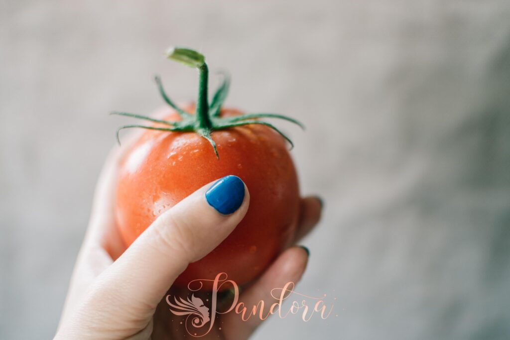 Vibrant red tomato held in a hand with blue nail polish, emphasizing freshness — Pandora Nail Spa, Lafayette, CA