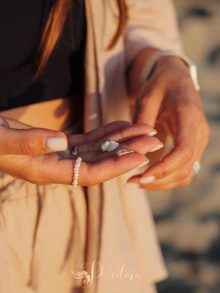 A close-up shot of a woman's manicured hands holding small beach stones and wearing a pearl ring — Pandora Nail Spa, Lafayette, CA
