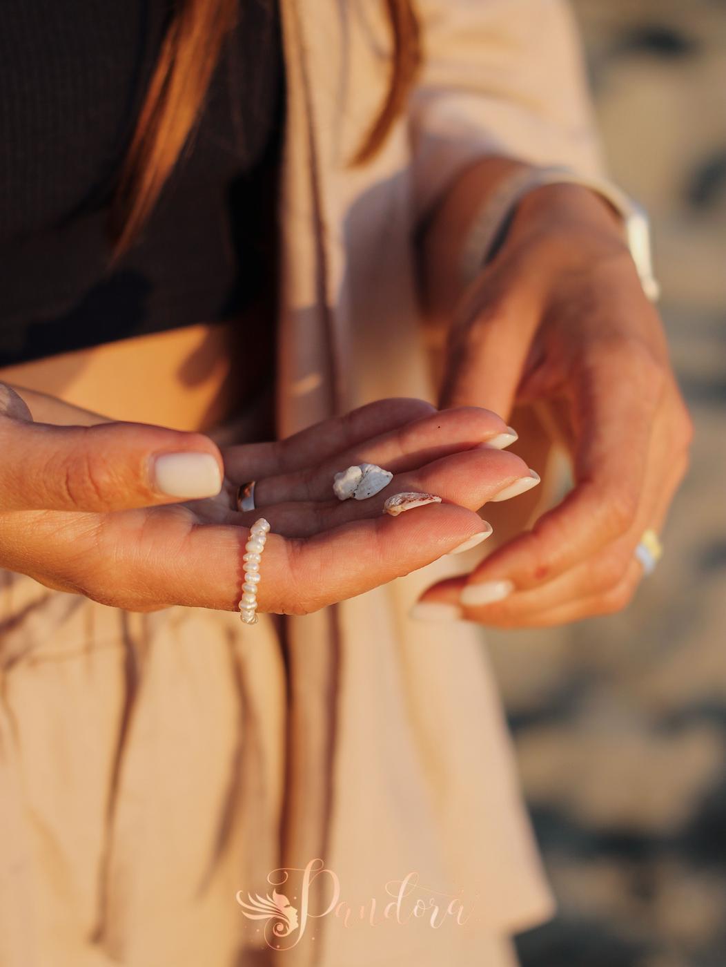 A close-up shot of a woman's manicured hands holding small beach stones and wearing a pearl ring — Pandora Nail Spa, Lafayette, CA