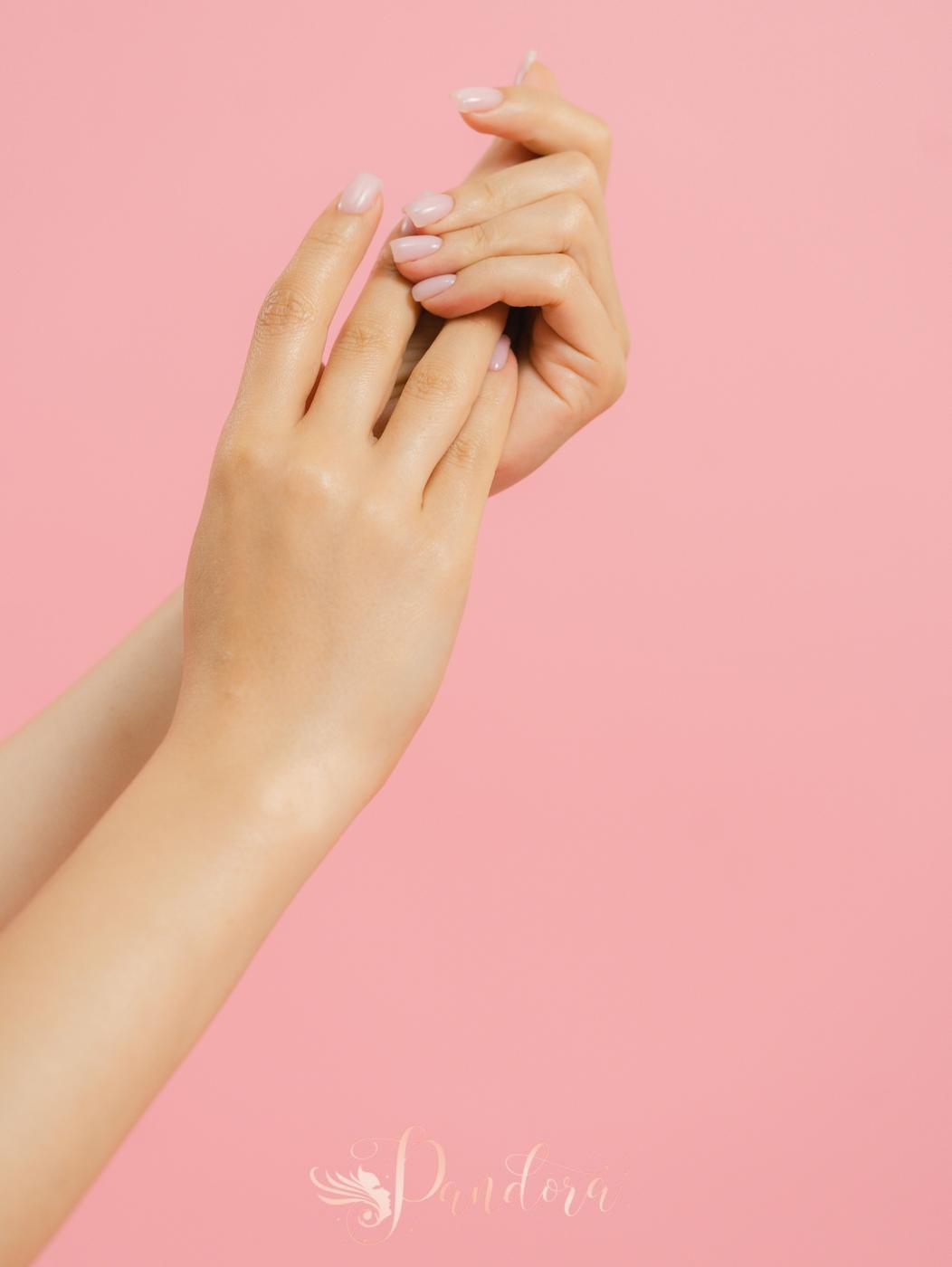 Close-up of elegant manicured hands with a pink background, showcasing nail care and beauty — Pandora Nail Spa, Lafayette, CA