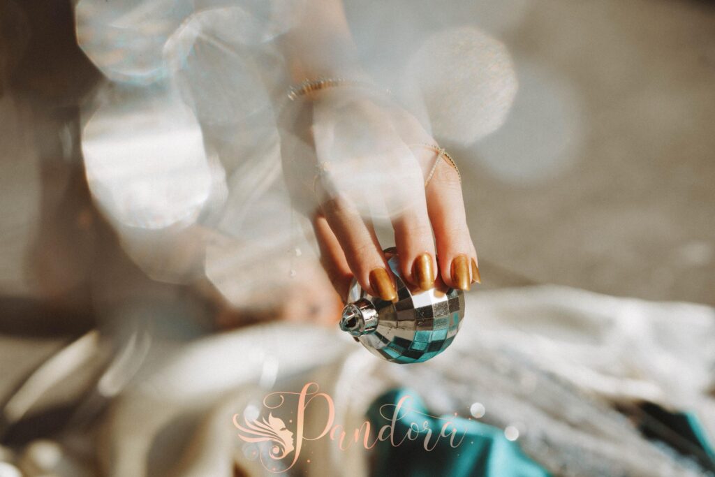 A close-up of a hand with manicured nails holding a shiny Christmas bauble, capturing holiday elegan — Pandora Nail Spa, Lafayette, CA