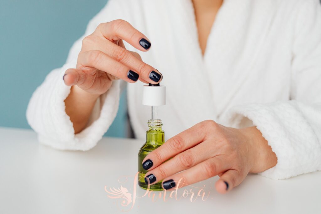 Close-up of a woman in a white bathrobe using a skincare product dropper with painted nails — Pandora Nail Spa, Lafayette, CA