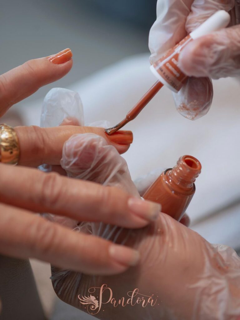 Detailed view of orange nail polish application during a manicure, showcasing precision and care — Pandora Nail Spa, Lafayette, CA